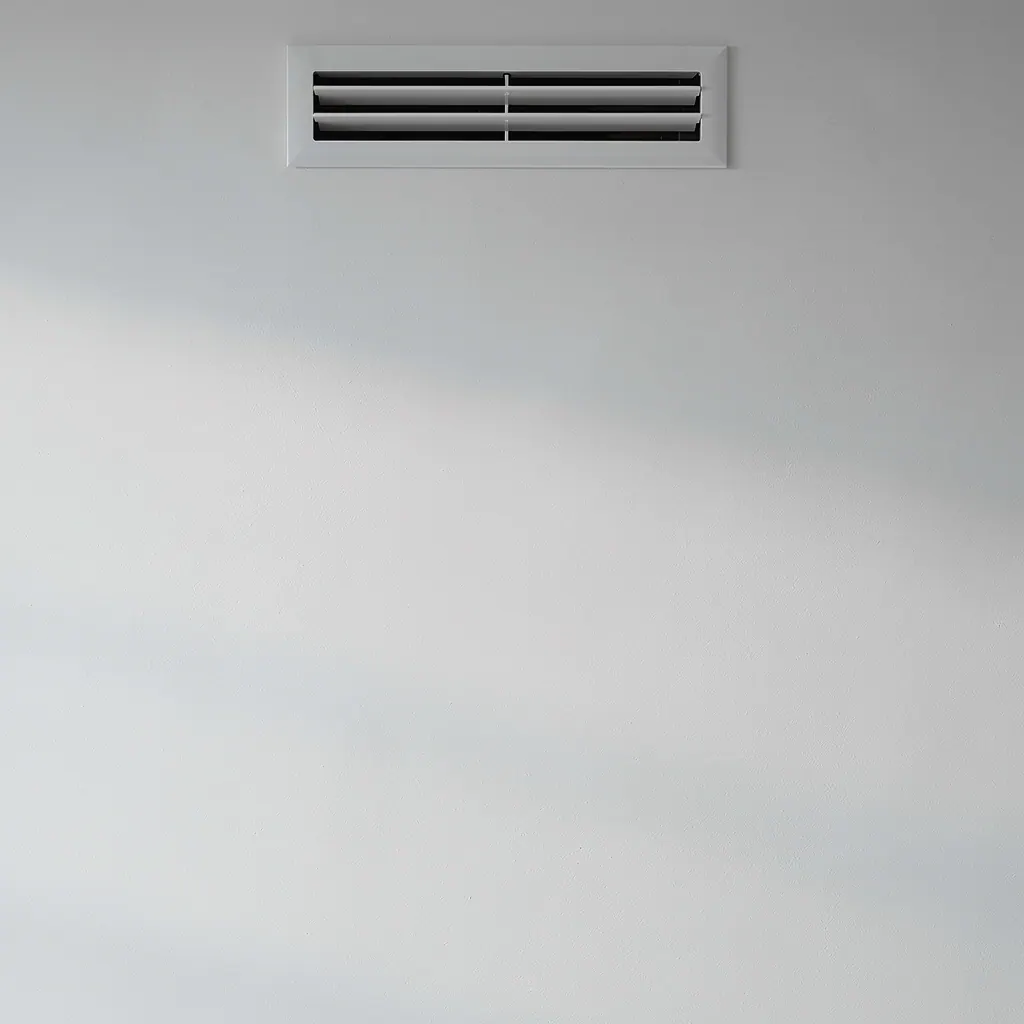 Vit innervägg med ventilationsdon i lugnt sidoljus, en av de tysta källorna till röklukt som ingen annan känner.